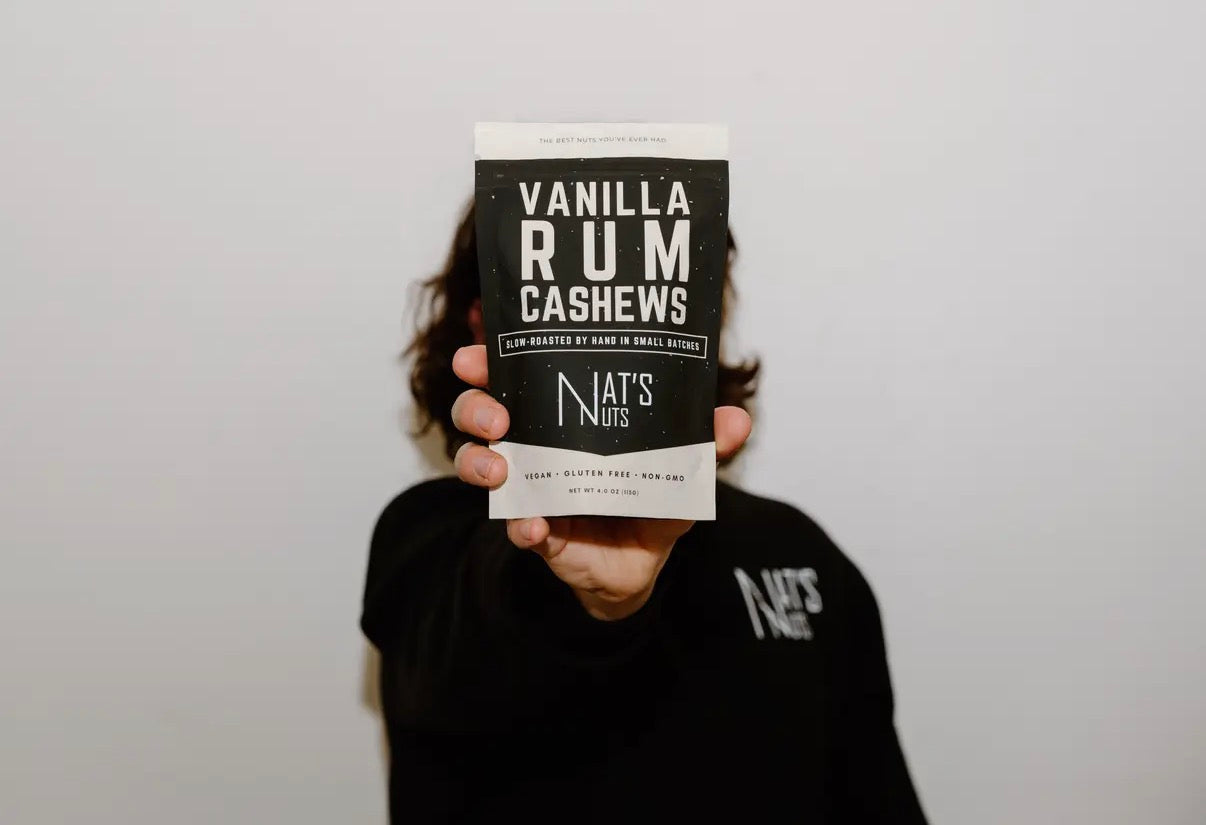 Person holding a package of Vanilla Rum Cashews by Nat's Nuts against a plain background